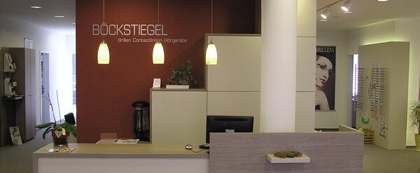 Modernes Optiker-Geschäft mit Empfangstresen, Brillenregalen und stilvoller Beleuchtung.